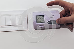 View of a hand adjusting the heating temperature. Digital thermostat on the wall of the house