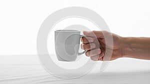 View of a hand holding a plain white ceramic mug against a light