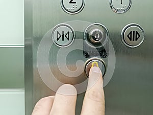 View of hand pressing emergency button on interior panel of an elevator