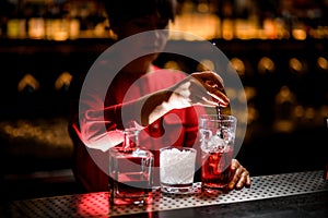 view on hand of woman bartender stirring by spoon drink with ice cubes in glass