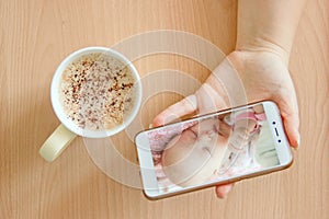 View handheld color video baby monitor. Female hands are holding a smartphone with a baby monitor app. Near hot drink