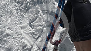 A view of the hands of a climber in black gloves, holding onto a jumar and climbing up the mountain on a rope