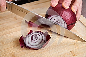 View on hands of a man chopping fresh red onion for lunch an a bamboo cutting board.