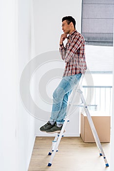 View of handsome african american man standing at ladder and looking at wall