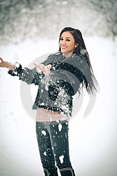 View of happy brunette girl playing with snow in winter landscape. Beautiful young female on winter background. Attractive woman