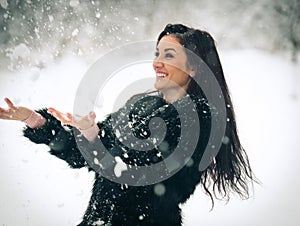 View of happy brunette girl playing with snow in winter landscape. Beautiful young female on winter background. Attractive woman