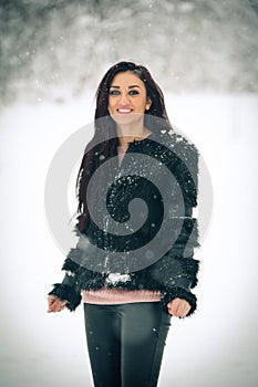 View of happy brunette girl playing with snow in winter landscape. Beautiful young female on winter background. Attractive woman