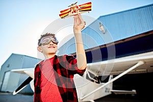 Happy kid playing with toy airplane near hangar, dreams to be a pilot