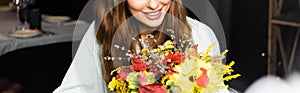View of happy woman with bouquet of autumn flowers in cafe