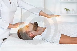 View of healer putting hands above head while healing handsome man on massage table