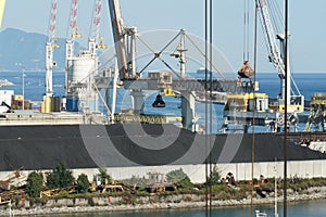 View on heaps of black coal loading and discharging by gantry cranes with grab in port of Genoa.