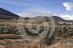 View of a high-mountain village near a motley hill covered with sand and small stones from an abandoned quarry in Armenia.