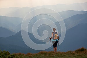 The view with the high mountains in fog. The sun rays are enlighten the forests. The extreme girl with the tracking sticks.