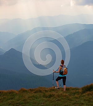 The view with the high mountains in fog. The sun rays are enlighten the forests. The extreme girl with the tracking sticks.