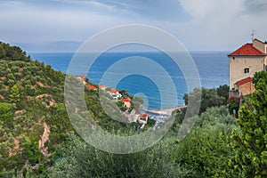 View from a high point of view on a green wooded ridge, small houses with red roof tiles.