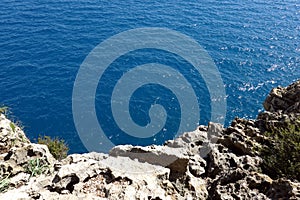View from high rocky shore to the azure transparent sea water with sunlight reflection in nnsunny day
