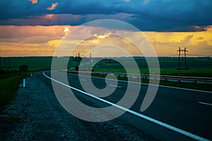 View of the highway, road, with car traffic in the evening against the background of a stormy sky with an orange sunset