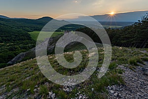 View of hill meadows and Spis Castle in the Slovak Little Carpathian Mountains with the setting sun in the background