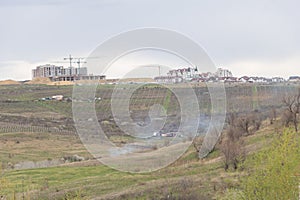 View from a hill of a new residential complex and vineyards in a sinking town in spring, with smoke coming out of