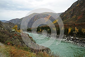 A view from the hill to the bend of a beautiful turquoise river flowing through an autumn valley in the mountains