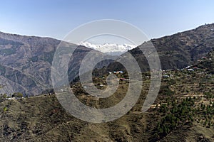 View of a Himalayan village on slop of mountain and snow capped mountain ranges