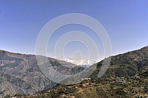 View of a Himalayan village on slop of mountain and snow capped mountain ranges