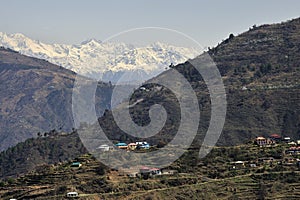 View of a Himalayan village on slop of mountain and snow capped mountain ranges