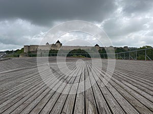 View of the historic Ivangorod castle from a wooden deck, set against a cloudy and dark sky