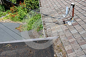 View from house rooftop of roof shingles, gutters, tree debris, moss, utility lines, driveway and garden