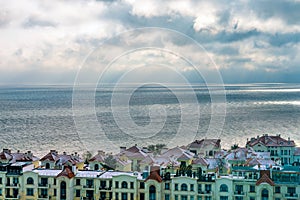 View of houses and rooftops against the backdrop of the sea in cloudy weather, the sun`s rays make their way through the dramatic