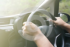 view of human hands holding steering wheel driving a car on a city street on a mist sunny day
