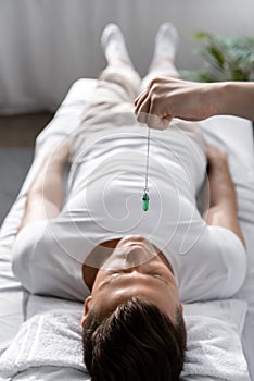 View of hypnotist standing near man on massage table and holding green stone