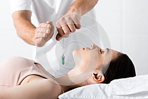 View of hypnotist standing near woman on pillow and holding green stone