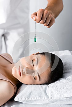 View of hypnotist standing near woman on pillow and holding green stone