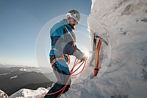 view of ice axe and man climber with equipment and ropes on the slope against backdrop of sky