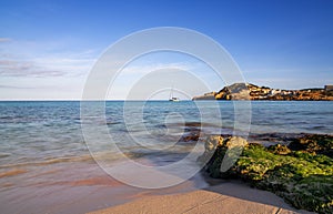 view of the idyllic bay and beach of Cala Agulla in eastern Majorca with a sailboat in the foreground