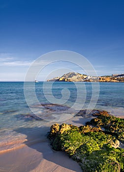 view of the idyllic bay and beach of Cala Agulla in eastern Majorca with a sailboat in the foreground