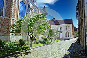 View on idyllic medieval cobblestone street, church garden, residential old homes, blue sky