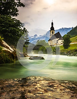 View of the idyllic St. Sebastian church in Ramsau in summer, wooden bridge leads over a mountain stream, Bavaria, Germany