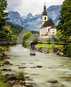 View of the idyllic St. Sebastian church in Ramsau in summer, wooden bridge leads over a mountain stream, Bavaria, Germany