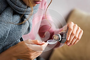 View of ill woman with grey scarf taking cough syrup