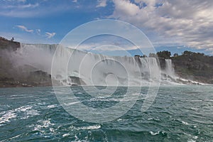 View of the impressive Niagara Falls. US falls from the Canadian side of Niagara. Massive water falls under the cloudy sky. Spume