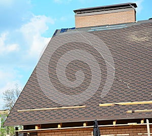 A view on an incomplete roof with asphalt shingles installation on the waterproof underlayment. Asphalt shingle tiles at the ridge photo