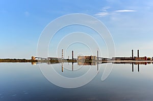 View of an industrial plant with chimneys and workshop buildings near the lake against blue sky. Cleaning Up after pollution. Safe