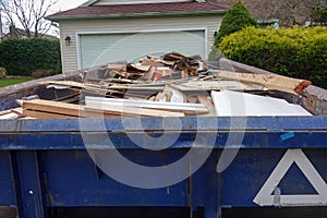 View inside a blue dumpster full of construction debris in front of a garage door