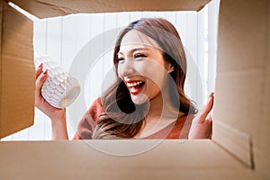 View from inside the box, a smiling woman unpacking awaited parcel, holding a vase, sitting with satisfied. Happy customer opening