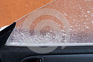 View from the inside of the car, during the first frost, through the powdered and frozen glass with ice. foreground and background