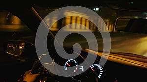 View from inside the car of man hands driving a vehicle at night. Stock footage. Moving along buildings, trees, and