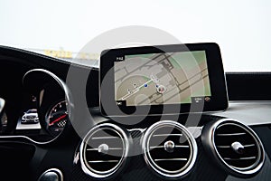 View from inside a car on a part of dashboard with a navigation unit and blurred street in front of a car