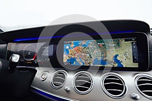 View from inside a car on a part of dashboard with a navigation unit and blurred street in front of a car